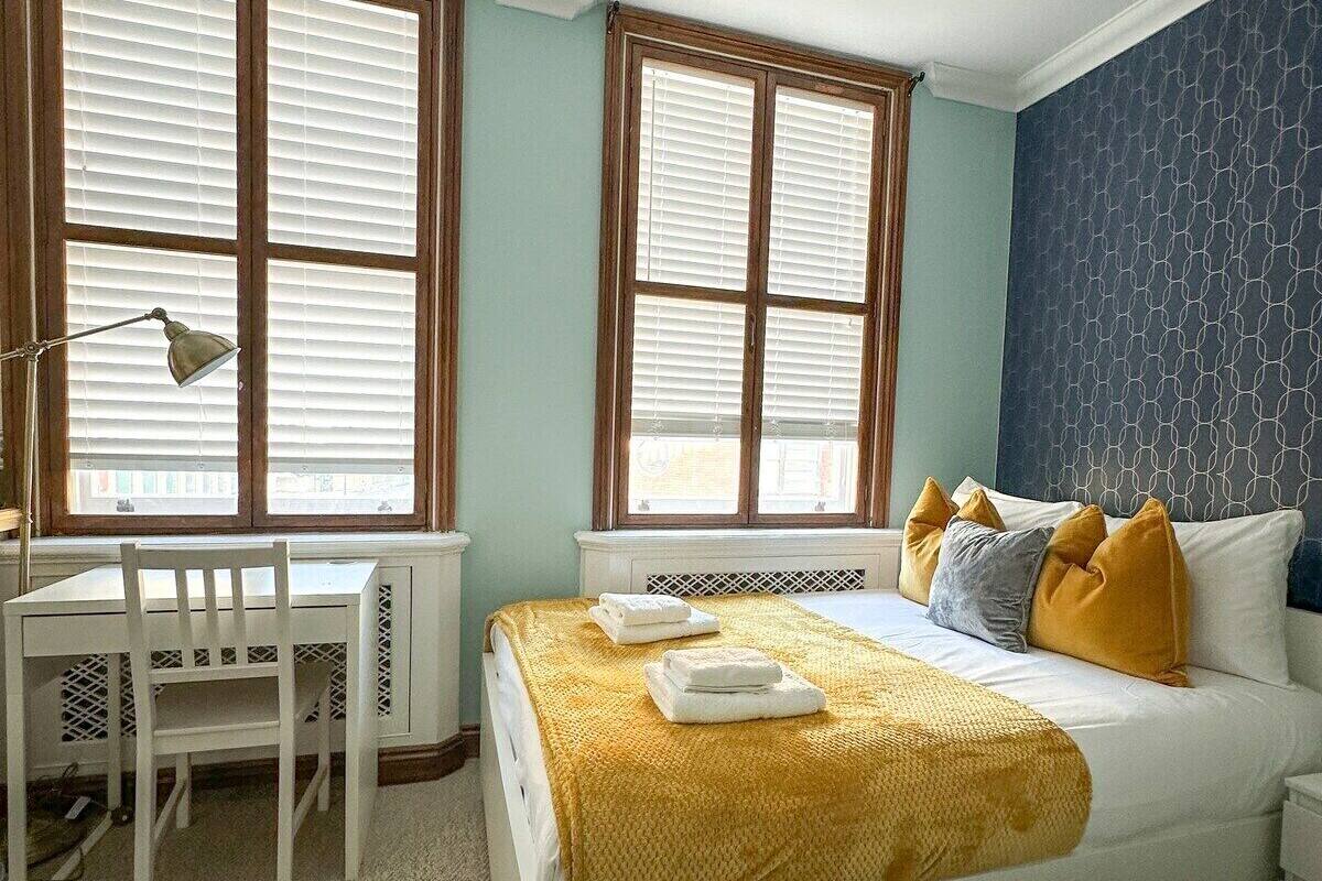 Une chambre à coucher avec un lit, un bureau et deux fenêtres équipées de stores.