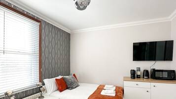 Une chambre moderne équipée d’un lit, de tables de chevet, d’un téléviseur à écran plat, d’un four à micro-ondes et d’une machine à café.
