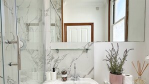 A bathroom with a glass shower enclosure, a white sink, a mirror, and a window. - Fulham Rooms (London)