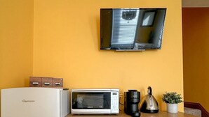 A compact kitchenette with a white fridge, a microwave, a coffee maker, and a small potted plant. - Fulham Rooms (London)