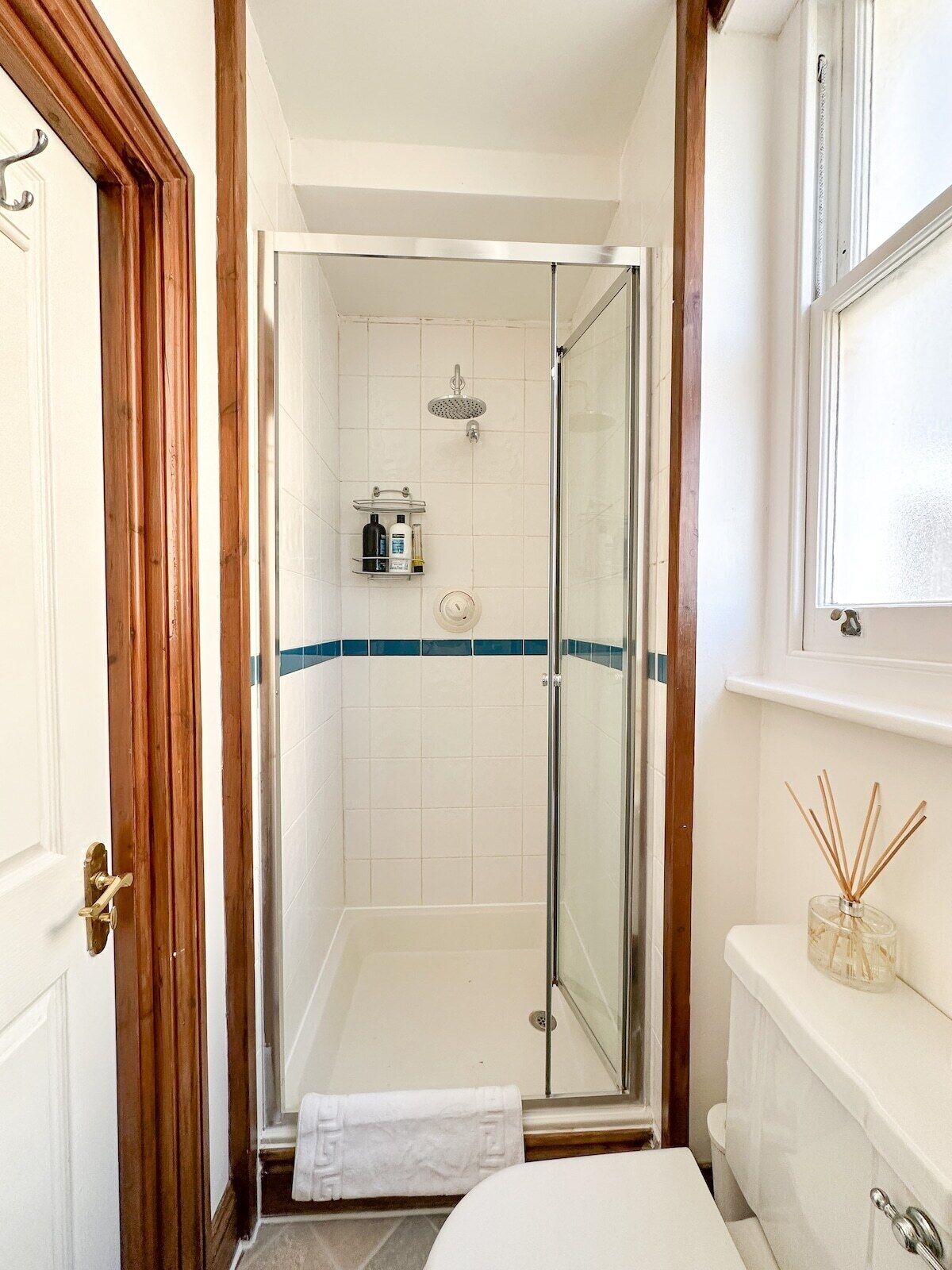 A bathroom with a glass-enclosed shower, a white toilet, and a window above the sink.