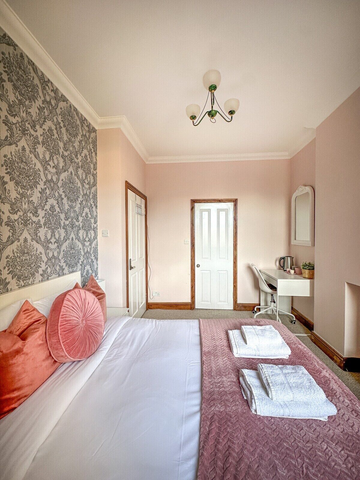 A bedroom with a bed, a desk, a chair, a mirror, and a door.