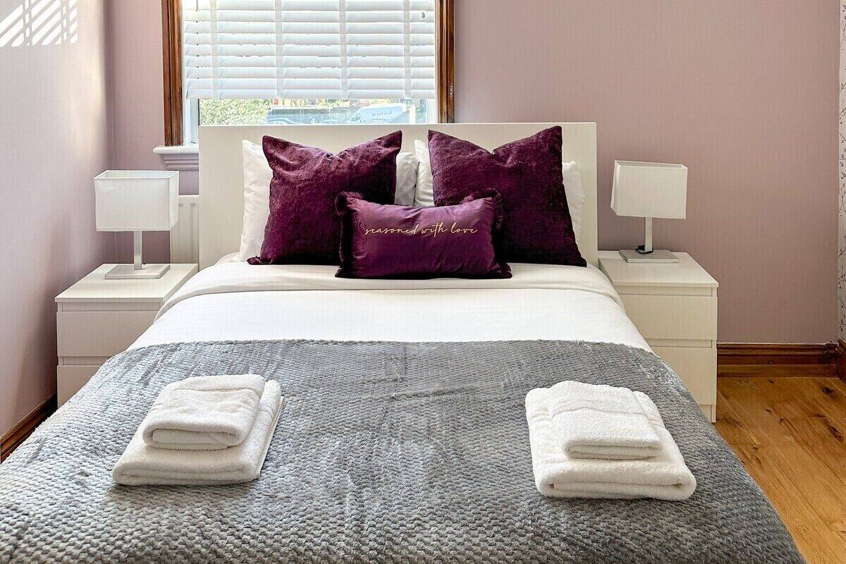 Une chambre à coucher avec un lit, deux tables de chevet, une fenêtre avec des stores et une vue sur l’extérieur.