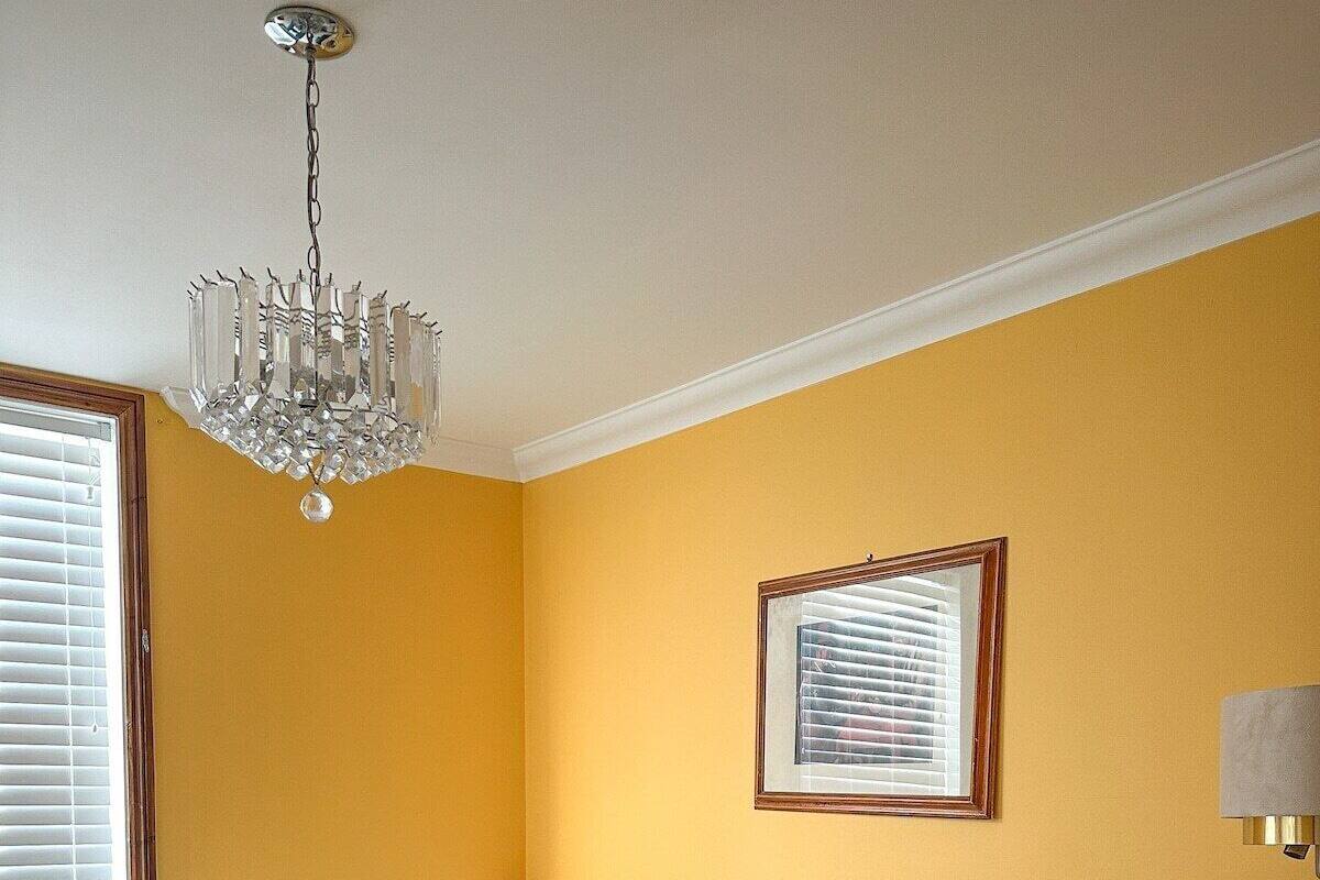 Une chambre d’hôtel avec deux lits simples, un lustre, un tableau encadré au mur et une table de chevet avec une lampe.