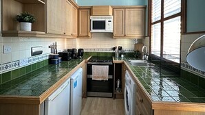 A compact kitchen with wooden cabinets, a microwave, a sink, and a washing machine. - Fulham Rooms (London)
