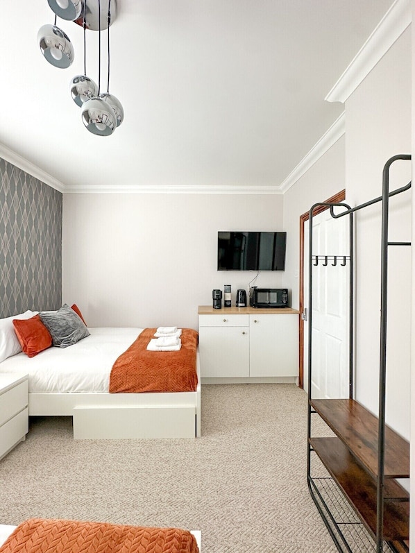 Una habitación de hotel moderna con una cama, un televisor, una cafetera y un perchero metálico.