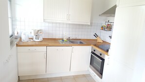 A kitchen with white cabinetry, a coffee maker, a sink, and a stove. - Apartment 'Fewo Mühlenstr Mit Terrasse' with Private Terrace, Private Garden and Wi-Fi (Prerow)