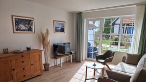 A living room with a wooden cabinet, a television, a sofa, and a view of the outside. - Apartment 'Fewo Mühlenstr Mit Terrasse' with Private Terrace, Private Garden and Wi-Fi (Prerow)