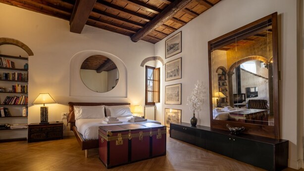 Ein Schlafzimmer mit Holzboden, einem Bett mit Kopfteil, einem Nachttisch, einer Lampe, einer Kommode, einem Spiegel und gerahmten Bildern an der Wand.