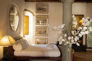 A hotel room with a bed, a nightstand with a lamp, a vase with white flowers, and framed pictures on the wall. - Monalda Tower Apartment (Firenze)