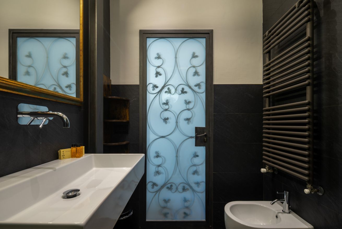 A modern bathroom with a large white sink, a smaller sink, and a glass partition with decorative patterns.