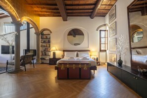 Quarto com piso de madeira, uma cama grande, cômoda, estante e espelho redondo na parede.