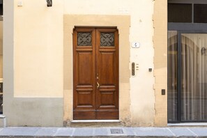 A double wooden door with decorative glass panels, a beige wall, and a black-framed window to the right. - Monalda Tower Apartment (Firenze)