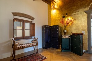 A room with a bench, a window with wooden shutters, a wall-mounted lamp, and a vase with flowers. - Monalda Tower Apartment (Firenze)