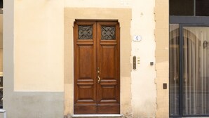Eine doppelte Holztür mit dekorativen Glasscheiben, eine beige Wand und ein rechts befindliches Fenster mit schwarzem Rahmen.
