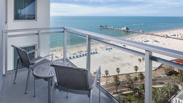 Un balcon avec vue sur une plage, une jetée et des palmiers.