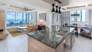 Un intérieur moderne avec un îlot de cuisine, un coin repas et un espace détente près d’une grande fenêtre donnant sur la mer.
