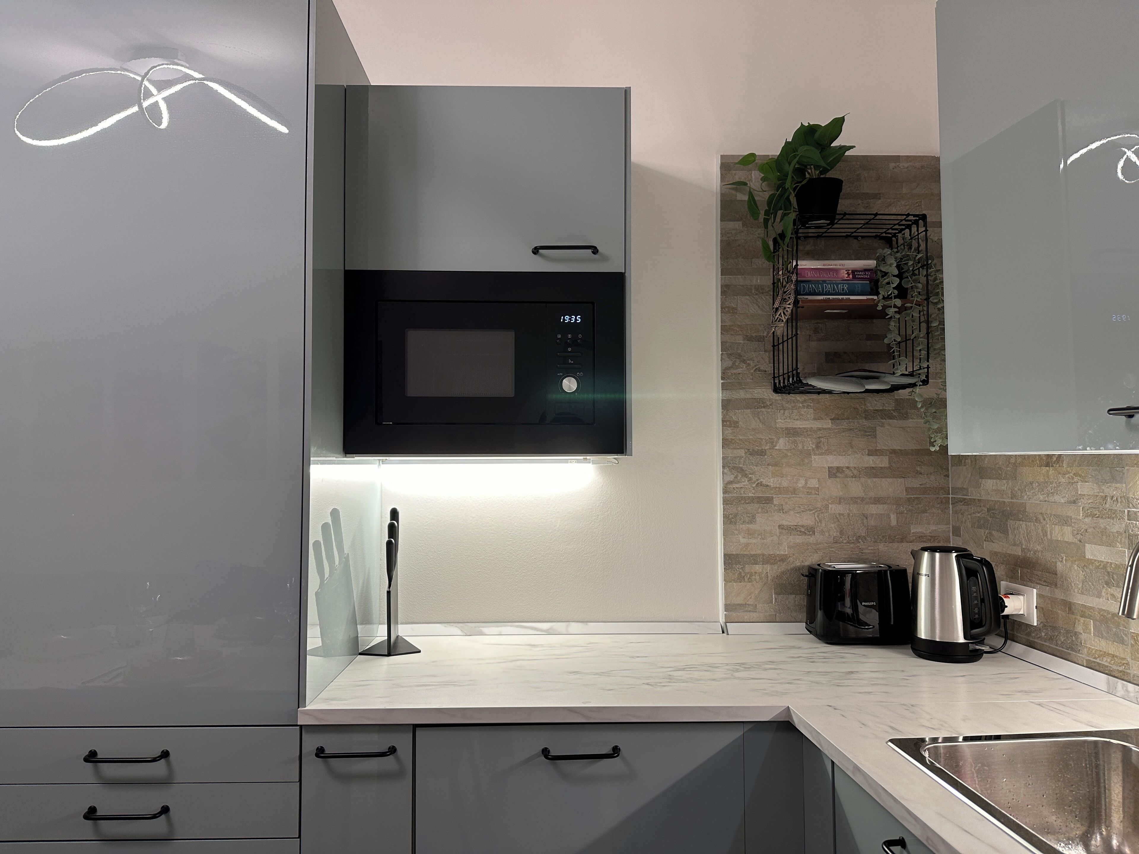 A modern kitchen with a built-in microwave, a coffee maker, and a plant on the wall.