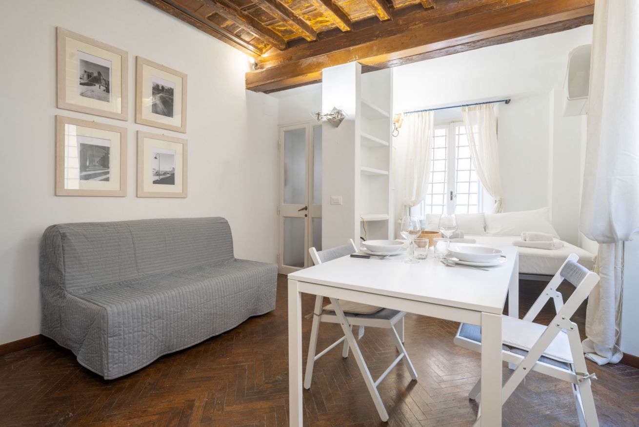 A room with a white sofa, a dining table with chairs, and four framed pictures on the wall.