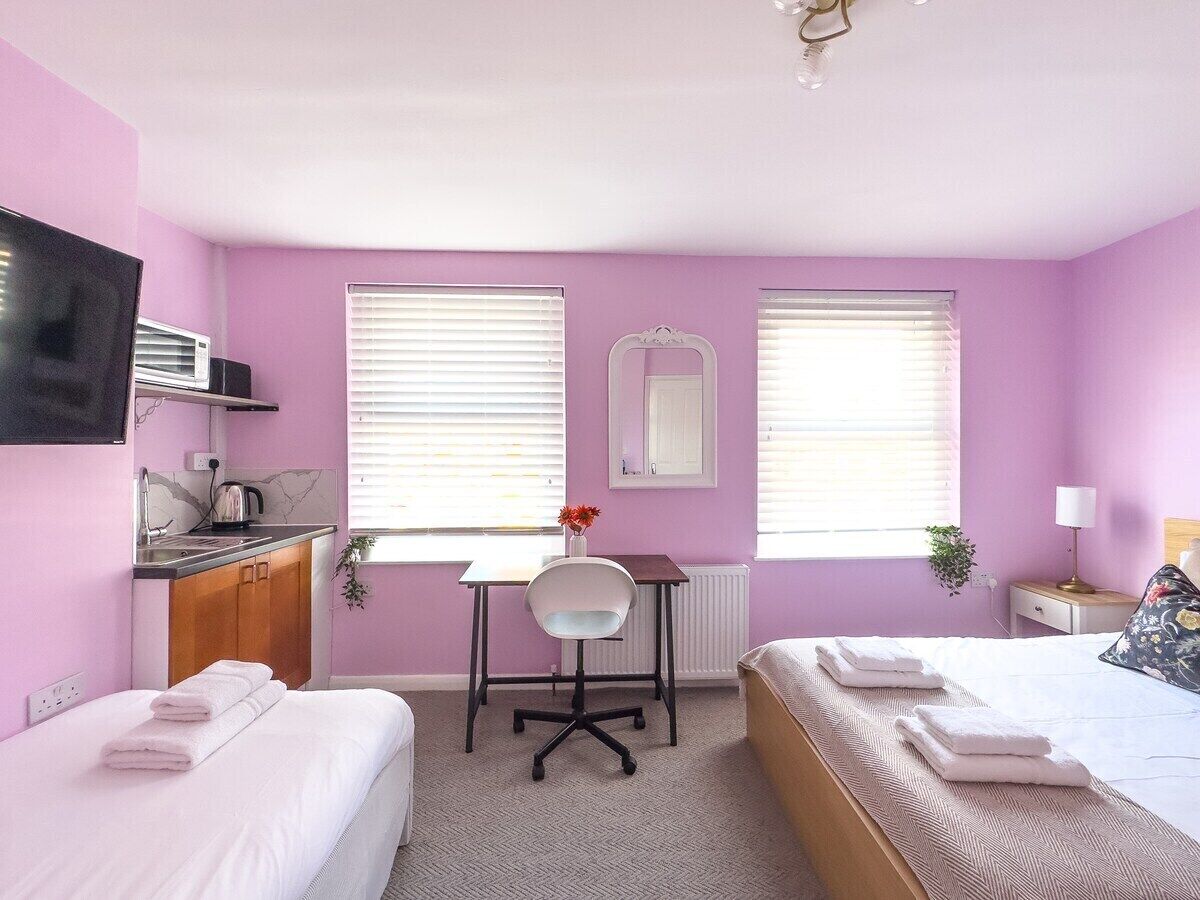 Une chambre avec deux lits, un bureau, une chaise, une télévision et une fenêtre avec des stores.