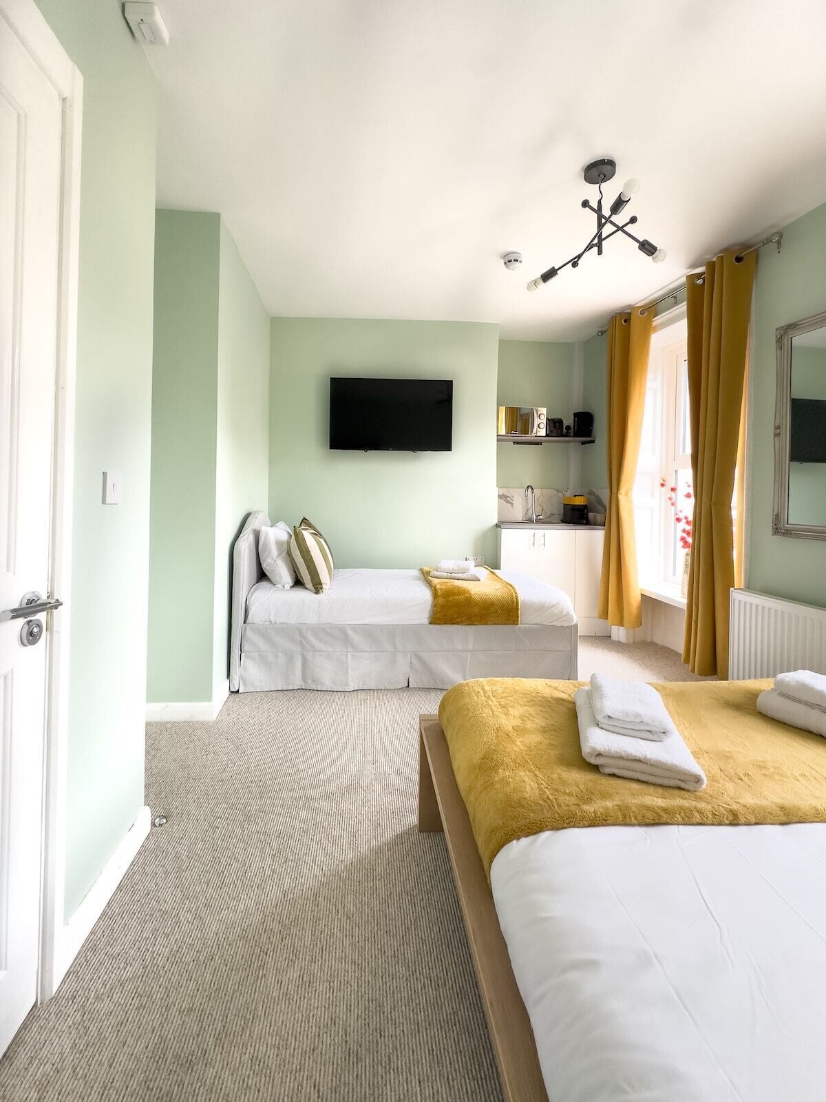 Ein Hotelzimmer mit zwei Betten, einem Fernseher, einer Küchenzeile und einem Badezimmer.