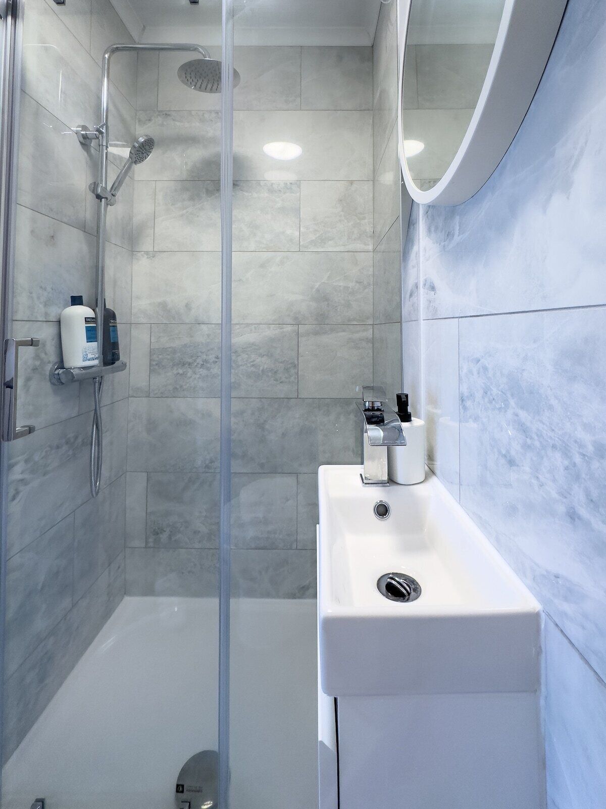 Un baño moderno con ducha de vidrio, lavamanos blanco y pared revestida de mármol.