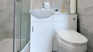 A modern bathroom with a glass shower enclosure, a round mirror, a white sink, and a toilet. - Camden Rooms (London)