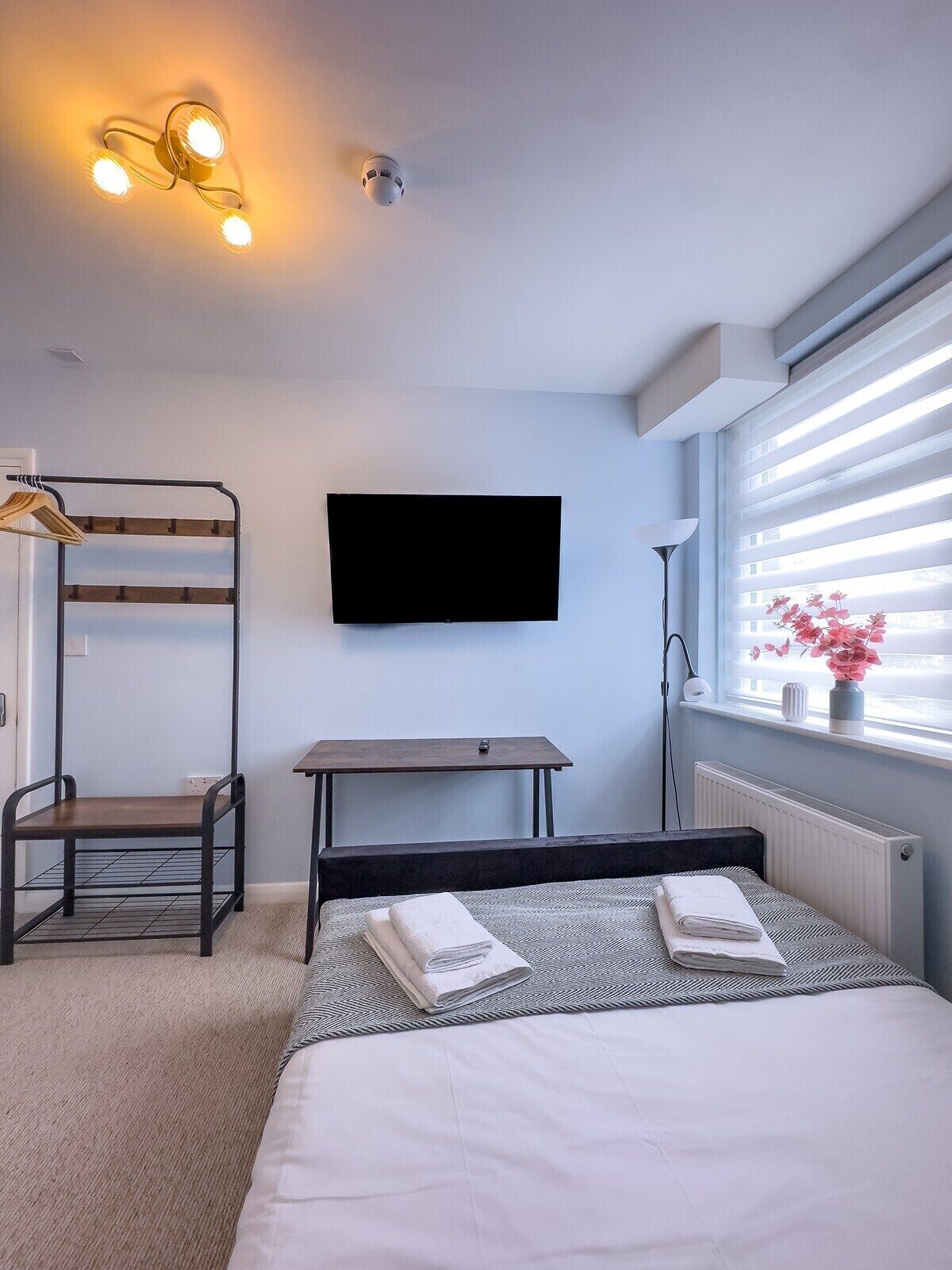 Une chambre moderne avec un lit superposé, un téléviseur à écran plat, une table de chevet et une fenêtre avec des stores.