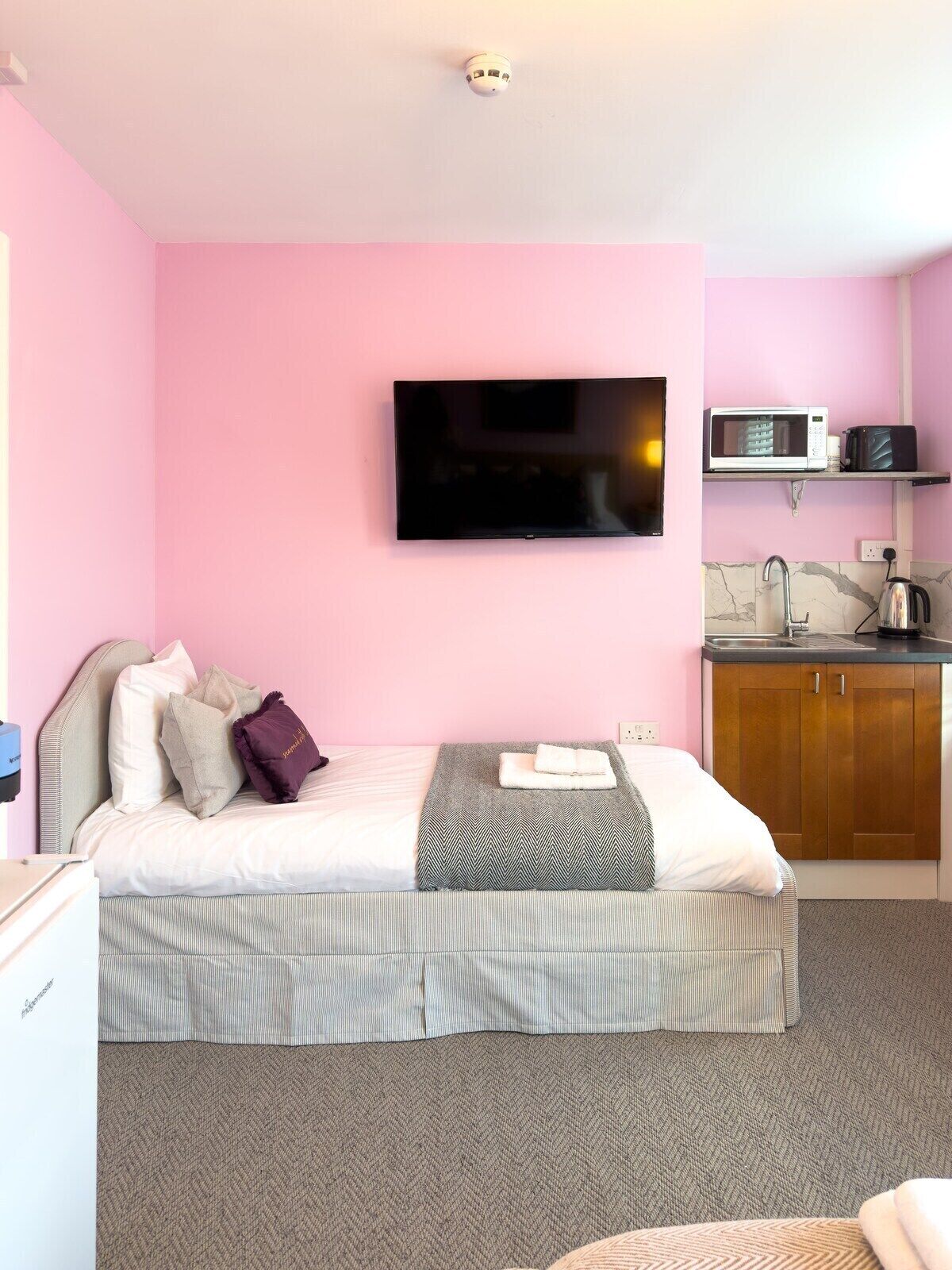 A bedroom with a bed, a flat-screen TV, a microwave, and a small kitchenette.