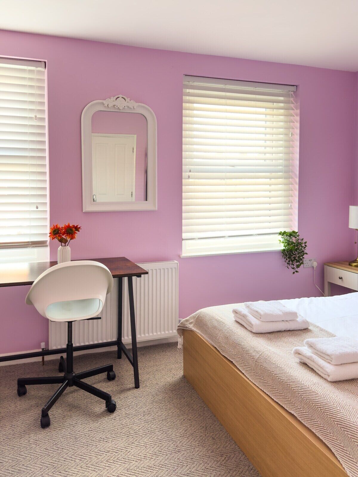 A bedroom with a bed, a desk, a chair, a radiator, and a window with blinds.