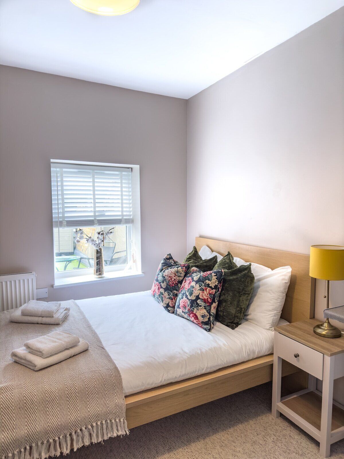 A bedroom with a bed, bedside table, lamp, window, and radiator.