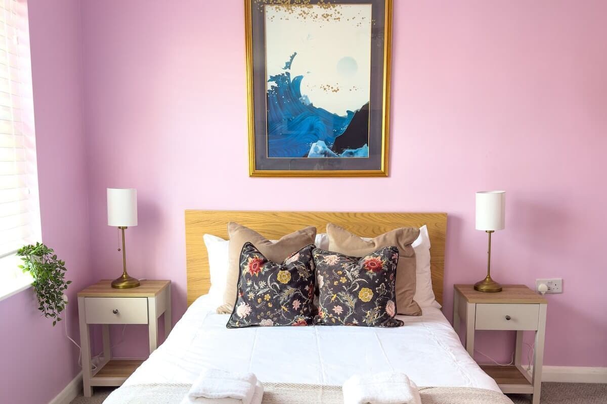 A neatly made bed with floral pillows, a framed artwork above it, and two bedside tables with lamps.