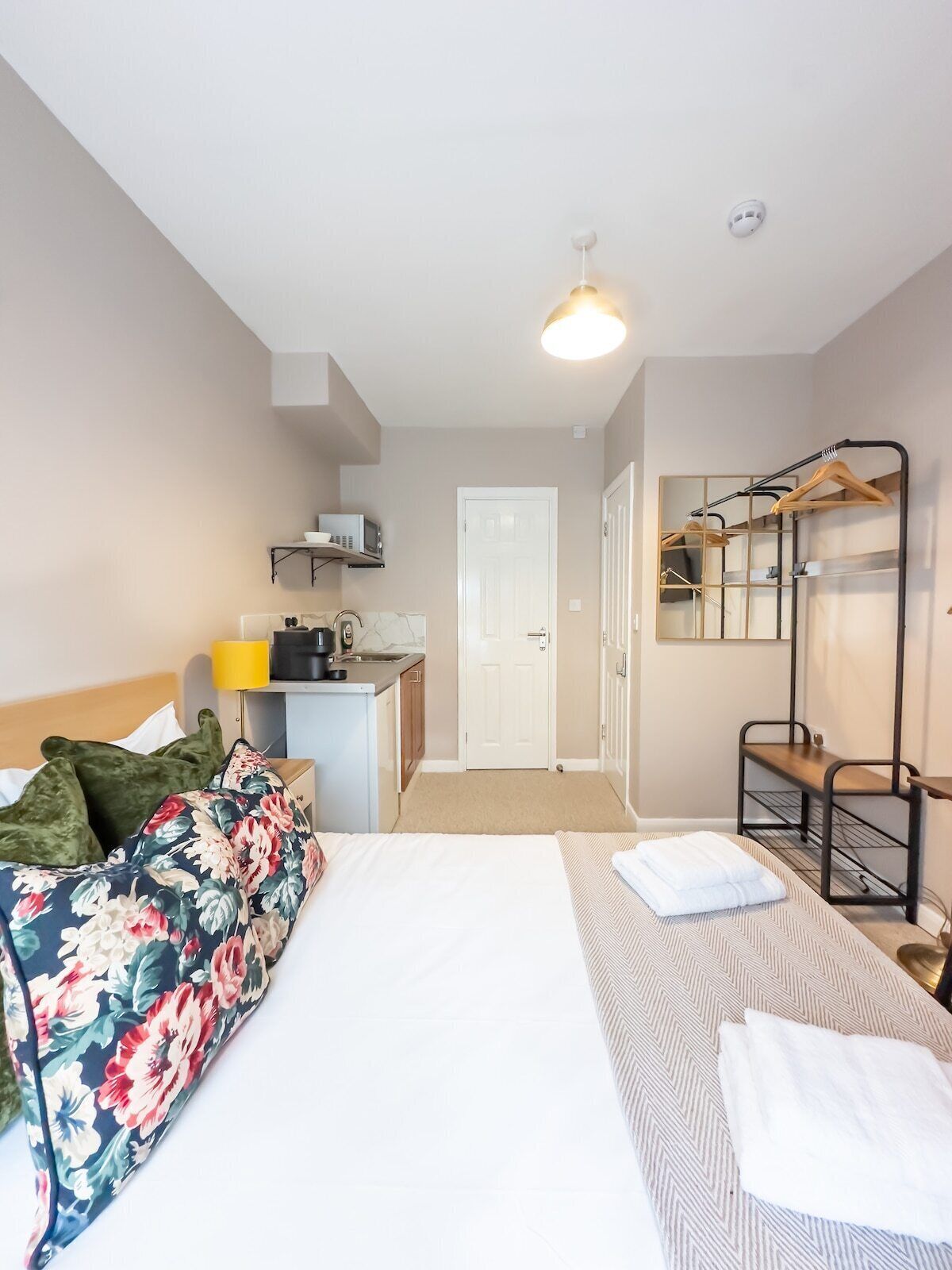 A compact hotel room with a bed, a desk with a microwave, a mirror, and a wardrobe.