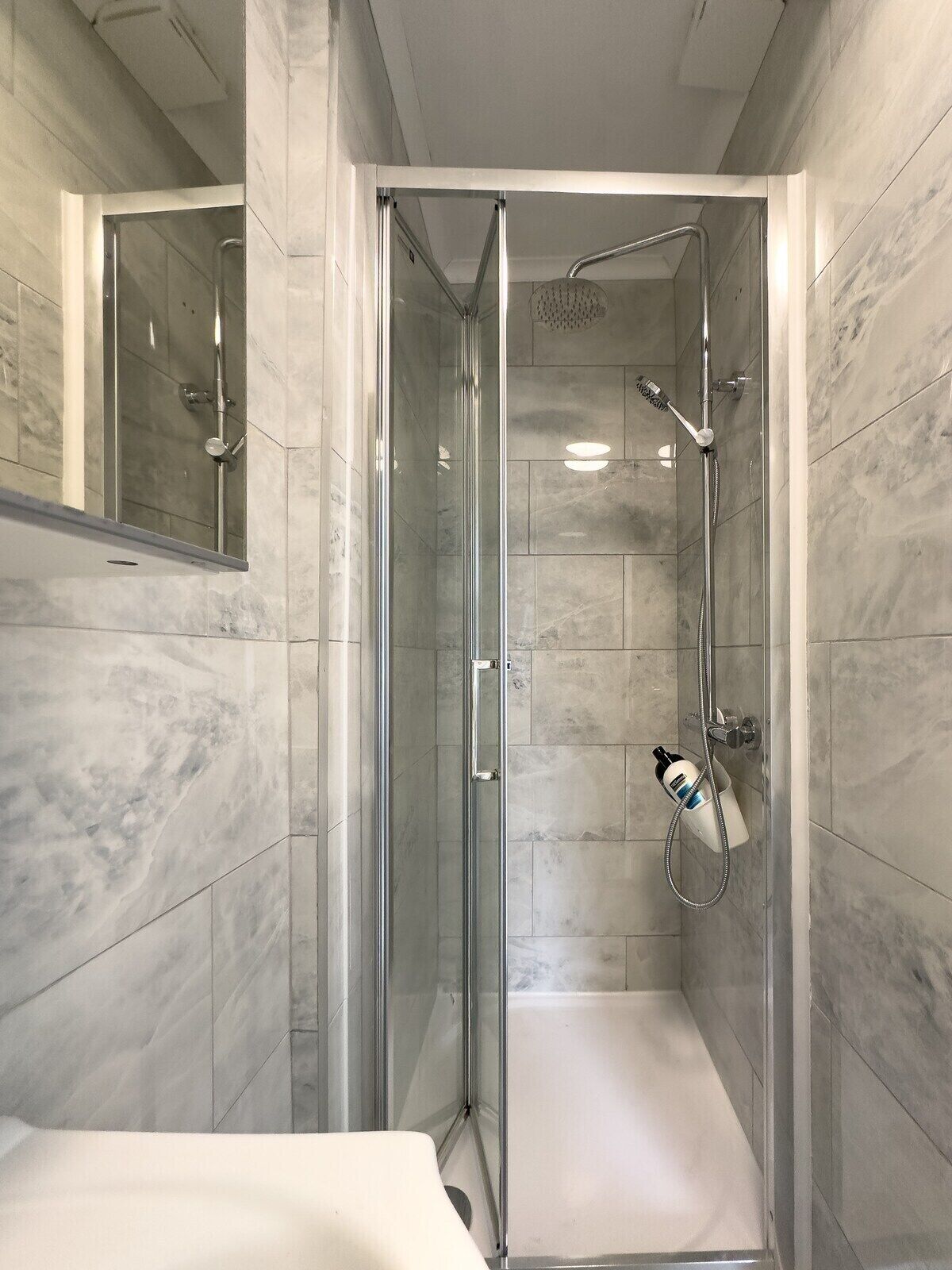 A modern shower with a glass door, a handheld showerhead, and a handheld shower attachment.