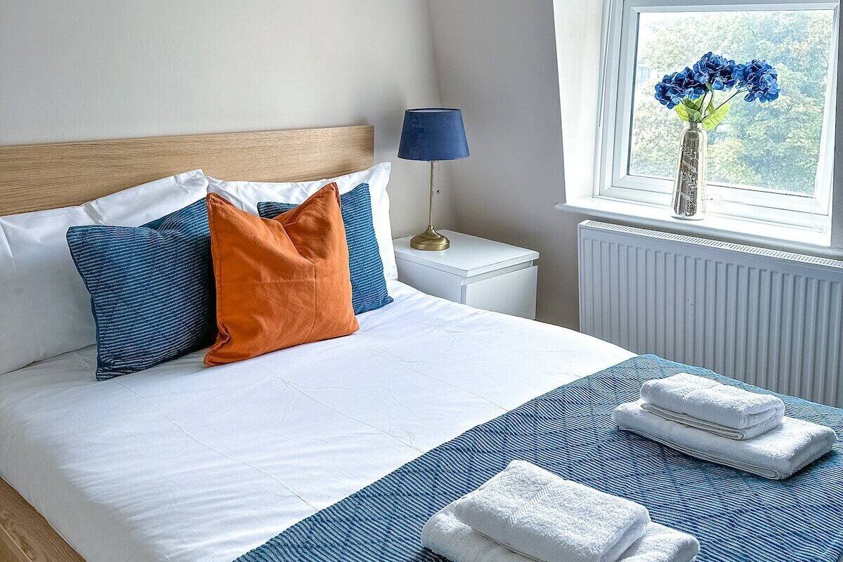 A bedroom with a bed, pillows, a bedside lamp, a window with a view, and a radiator.