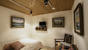 A bedroom with a bed, a TV, a table with a book and a glass of wine, and framed pictures on the walls.