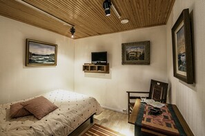 Makuuhuoneessa on sänky, televisio, pöytä, jonka päällä on kirja ja lasi viiniä, sekä seinillä on kehystettyjä valokuvia.