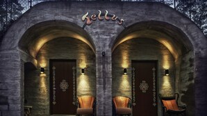 A stone building with two arched doorways, each with a light fixture and a chair in front.