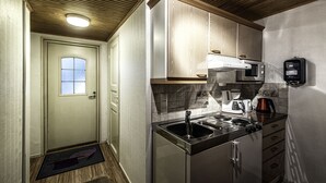 Une cuisine de taille réduite, équipée d’un évier, d’une cuisinière et d’un four à micro-ondes. On y trouve une porte avec une fenêtre et un paillasson sur le sol.
