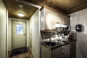 Una cocina compacta con un lavamanos, estufa y microondas. Hay una puerta con ventana y un felpudo en el piso.