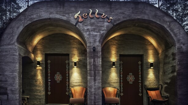 Un bâtiment en pierre doté de deux portes en arc, chacune étant agrémentée d’un luminaire et d’une chaise placée devant.