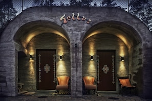 Un edificio de piedra con dos arcos de entrada, cada uno con una lámpara y una silla al frente.