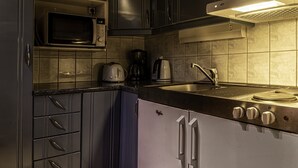 Une cuisine de taille réduite, dotée de meubles de rangement sombres, d’un four à micro-ondes, d’une bouilloire, d’une machine à café et d’un évier.