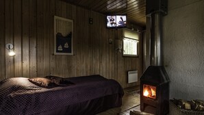 A cozy room with a bed, a fireplace, a television, and wooden walls.