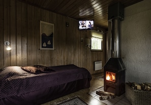 A cozy room with a bed, a fireplace, a television, and wooden walls. - Cabin-Garden view-Private Bathroom-Cottage-Mökki 6 (Västerskog)