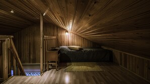 A wooden cabin bedroom with a bed, a nightstand, and a small table.