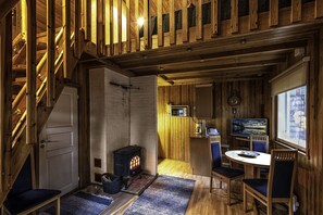 Ein gemütliches Blockhaus-Interieur mit einer Holztreppe, einem Kamin, einer Essecke mit Stühlen und Tisch sowie einem Fernseher.