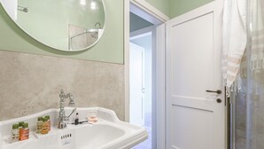A bathroom with a white sink, a mirror, and a door leading to another room. - Appartamento delle Logge (Cortona)