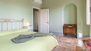A bedroom with a bed, a nightstand, a wooden dresser, a door, and a tiled floor. - Appartamento delle Logge (Cortona)