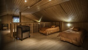 A cozy attic bedroom with wooden walls and ceiling, two beds, a wicker chair, and a small window. - Cabin-Garden view-Private Bathroom-Deluxe-Mökki 12,The Biggest Yell (Västerskog)